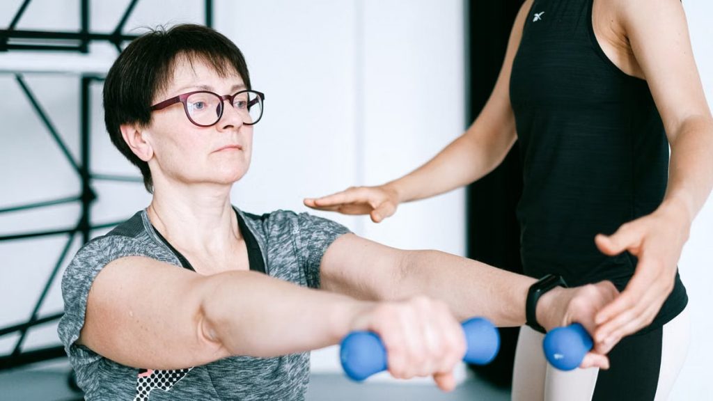 A personal trainer guides a woman in exercising with dumbbells for fitness and strength training.